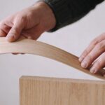 artisan courbe une fine feuille de bois sur un panneau