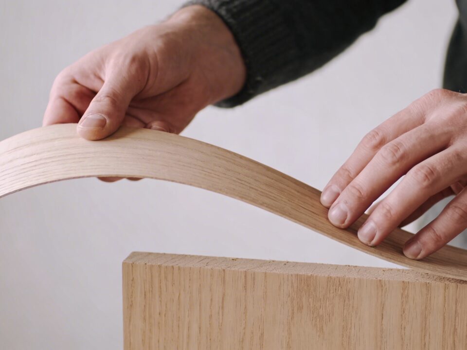 artisan courbe une fine feuille de bois sur un panneau