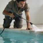 Homme penche nettoyant margelle piscine au nettoyeur haute pression