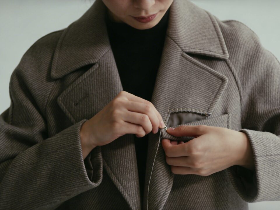 Personne debout decousant soigneusement la poche cousue dun manteau élégant